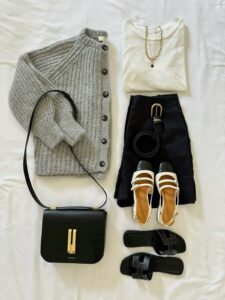 flatlay of capsule wardrobe pieces including a gray sweater, black skirt, sandals, necklace, and crossbody bag
